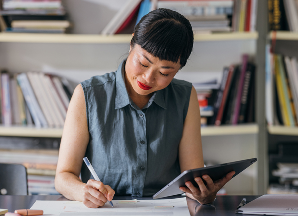 A smiling Japanese entrepreneur taking some notes while holding her tablet